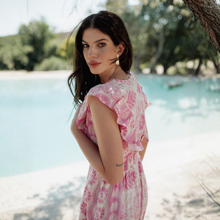 Load image into Gallery viewer, Woman in a pink dress standing by a body of water with trees in the background