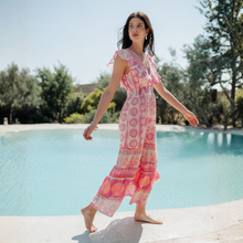Load image into Gallery viewer, Woman in a pink floral dress standing by a pool with trees in the background