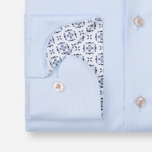 Load image into Gallery viewer, Close-up of a light blue striped dress shirt cuff with a patterned white and navy bandana pocket square tucked into the pocket.