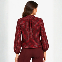 Load image into Gallery viewer, A woman shown from the back wearing a long-sleeve blouse with a red, black, and white geometric pattern, paired with burgundy pants, against a plain white studio background.
