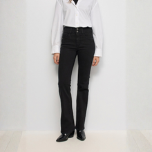 Load image into Gallery viewer, A model wearing black flared jeans, a white button-down shirt, and black leather shoes, standing against a plain white studio wall.
