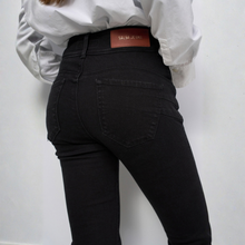 Load image into Gallery viewer, A person wearing black skinny jeans and a white long-sleeve shirt, shown from the back against a plain light gray wall. The jeans have a brown leather patch at the back waistband with the brand name 'Salsa Jeans' visible.