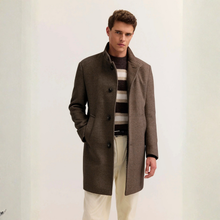 Load image into Gallery viewer, A man wearing a mid-length brown wool-blend overcoat over a dark striped sweater and cream trousers, standing against a plain off-white background.
