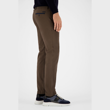 Load image into Gallery viewer, A side profile view of a person wearing slim-fit brown trousers, a dark navy long-sleeve shirt, and navy sneakers with white soles, set against a plain light gray studio background.