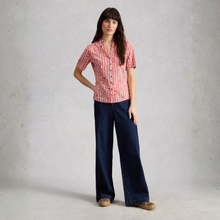 Load image into Gallery viewer, Woman wearing a red patterned shirt and blue jeans against a plain background