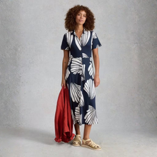 Load image into Gallery viewer, Woman wearing a navy dress with white leaf pattern, holding a red bag against a gray background