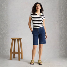 Load image into Gallery viewer, Woman wearing a black and white striped shirt and blue shorts standing next to a wooden stool against a gray background
