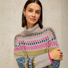 Load image into Gallery viewer, A woman wearing a multicolor Fair Isle knit turtleneck sweater with pink, blue, yellow, and gray patterns, posed against a textured beige wall.