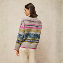 Load image into Gallery viewer, A woman shown from the back wearing a gray knit sweater with colorful Fair Isle style horizontal stripes in pink, blue, green, and yellow, paired with cream pants, set against a textured beige wall.
