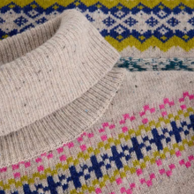 Load image into Gallery viewer, Close-up of a knit sweater showing a cream ribbed collar and body with multicolor Fair Isle patterns in blue, yellow, and pink.
