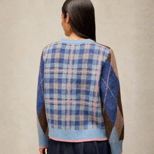 Load image into Gallery viewer, A woman viewed from behind wearing a fuzzy knit sweater with a blue, pink, and brown plaid back and argyle sleeves, set against a neutral textured beige wall.