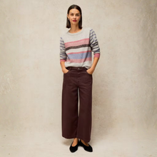 Load image into Gallery viewer, A woman stands against a textured beige wall wearing a gray knit sweater with pink, purple, and black horizontal stripes, paired with dark brown wide-leg trousers and black flats.