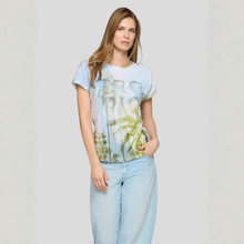 Load image into Gallery viewer, Woman wearing a light blue t-shirt with a nature print and light blue jeans on a plain background