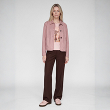 Load image into Gallery viewer, A model stands against a light gray studio background wearing a dusty pink cropped jacket over a pink graphic T-shirt, dark brown wide-leg trousers, and light pink slip-on shoes.