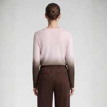 Load image into Gallery viewer, A woman viewed from the back wearing a long-sleeve knit top with a soft ombré fade from pale blush pink at the shoulders to dark brown at the sleeves and hem, paired with dark brown wide-leg pants, against a light gray studio background.