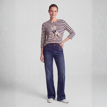 Load image into Gallery viewer, A woman modeling a navy and beige striped long-sleeve top with a dog graphic, paired with dark blue jeans and white shoes, against a light gray studio background.