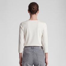 Load image into Gallery viewer, A woman models a cream long-sleeve top, paired with gray jeans against a light gray studio backdrop.