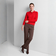 Load image into Gallery viewer, A woman modeling a bright red long-sleeve polo sweater and brown trousers, standing in a minimalist studio setting with light gray walls and floor.