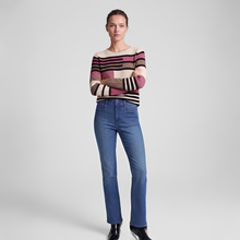 Load image into Gallery viewer, A model stands against a light gray studio background wearing a long-sleeve knit sweater with horizontal stripes in beige, brown, pink, and black, paired with blue jeans and black ankle boots.