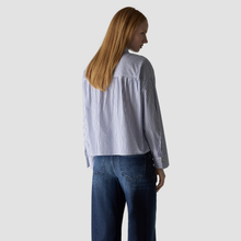 Load image into Gallery viewer, A woman with long red hair is shown from the back wearing a blue and white vertically striped long-sleeve blouse tucked into dark blue jeans, set against a solid light gray background.