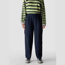 Load image into Gallery viewer, A model wearing navy blue wide-leg cargo pants, a lime green and navy striped long-sleeve top, and silver sneakers, shown from the chest down against a light gray studio background.