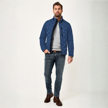 Load image into Gallery viewer, A man modeling a blue quilted jacket with a black zipper, worn over a gray sweater and blue jeans, standing against a plain white studio background.