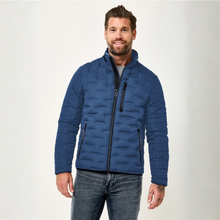 Load image into Gallery viewer, A man wearing a blue quilted puffer jacket with black zippers, paired with gray jeans, standing against a light gray studio background.