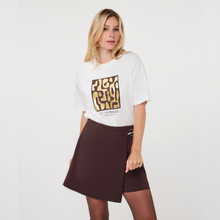 Load image into Gallery viewer, A woman modeling a white graphic T-shirt and a dark brown wrap-style mini skirt against a plain light gray studio background.