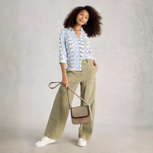 Load image into Gallery viewer, Woman wearing a floral blouse and beige pants, holding a beige handbag against a plain background