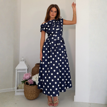 Load image into Gallery viewer, Woman wearing a navy blue dress with white polka dots in an indoor setting.