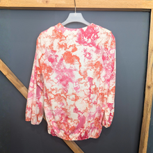 Load image into Gallery viewer, Floral patterned blouse on a hanger against a dark wall.