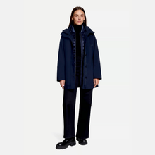 Load image into Gallery viewer, A model stands against a light gray studio background wearing a dark navy hooded coat over a black outfit with dark wide-leg trousers and black shoes.