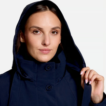 Load image into Gallery viewer, A close-up of a woman wearing a dark navy hooded jacket with a high collar and dark buttons, holding the edge of her hood against a light gray studio background.