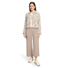 Load image into Gallery viewer, A model stands against a plain white studio background wearing a cropped tweed jacket in a beige and gray marled pattern, paired with wide-leg taupe trousers and cream sneakers.