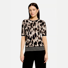 Load image into Gallery viewer, A woman modeling a short-sleeve knit top with an abstract black, brown, and beige pattern, featuring black and white horizontal stripes at the hem, against a light gray background.