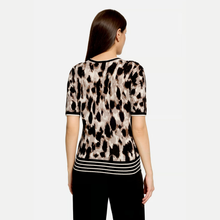 Load image into Gallery viewer, A woman viewed from the back wearing a short-sleeve knit top with a beige, brown, and black leopard print and white horizontal stripes at the hem, paired with black pants, against a light gray background.