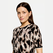 Load image into Gallery viewer, A woman wearing a short-sleeve knit top with a brown, black, and beige animal print pattern, photographed against a light gray studio background.