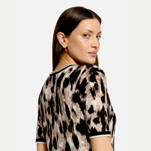Load image into Gallery viewer, A woman wearing a short-sleeve top with a brown, black, and beige animal print, photographed against a light gray studio background.