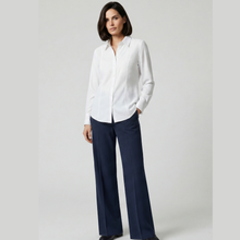 Load image into Gallery viewer, A woman modeling a white long-sleeve button-up shirt paired with navy wide-leg trousers, standing against a light gray studio background.