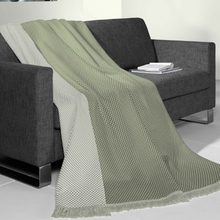 Load image into Gallery viewer, A sage green and off-white textured throw blanket with fringe is draped over a dark gray fabric sofa in a modern room setting.