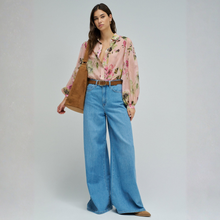 Load image into Gallery viewer, Woman wearing a floral blouse and blue jeans with a brown bag on a gray background