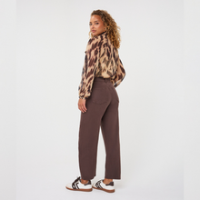 Load image into Gallery viewer, A woman stands in profile wearing a leopard-print long-sleeve blouse tucked into high-waisted, wide-leg brown trousers, paired with white and brown sneakers, against a plain white studio background.