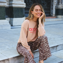Load image into Gallery viewer, Woman wearing a beige sweatshirt with 'Chicago' text and leopard print pants sitting on steps.
