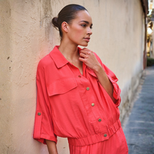 Load image into Gallery viewer, Posed image of a model wearing Esqualo SS Jacket in the colour Chili Red, with a busy background.