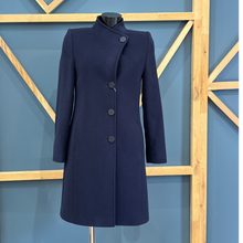 Load image into Gallery viewer, A dark navy blue wool coat with a high mock neck and asymmetrical button closure, displayed on a mannequin torso against a blue wall with a wooden geometric frame.