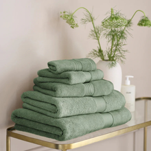 Load image into Gallery viewer, Stack of green towels on a gold metal shelf with a vase of greenery in the background.