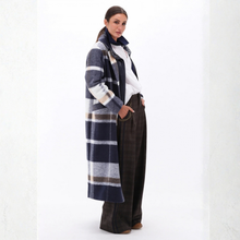 Load image into Gallery viewer, A woman models a long, navy blue and gray plaid coat over a white shirt and dark brown wide-leg trousers, standing against a white studio background.