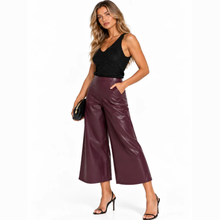 Load image into Gallery viewer, A woman modeling a pair of high-waisted, wide-leg cropped pants in a deep burgundy faux-leather finish, paired with a black sleeveless top and black high-heeled sandals.