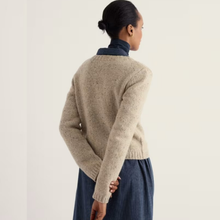 Load image into Gallery viewer, A woman shown from the back wearing a beige textured knit sweater over a dark navy mock neck top and a dark blue skirt, set against a plain off-white background.