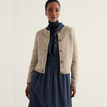 Load image into Gallery viewer, A woman modeling a beige knit cardigan over a navy blue turtleneck and matching navy dress, photographed against a plain off-white studio background.